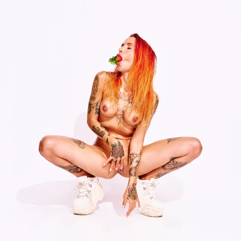 Nude art portrait of Ana Almeida featuring bright red hair, tattoos, and casual sneakers.